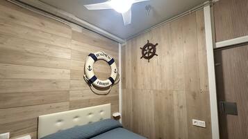 Une chambre à coucher avec un lit, des murs en bois, un ventilateur de plafond, une bouée de sauvetage et un décor représentant un gouvernail de navire.