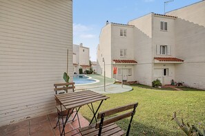 A residential area with white buildings, a swimming pool, and a patio with a table and bench.