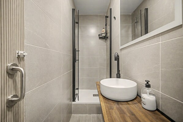 A modern bathroom with a glass shower enclosure, a white sink, and a wooden countertop.