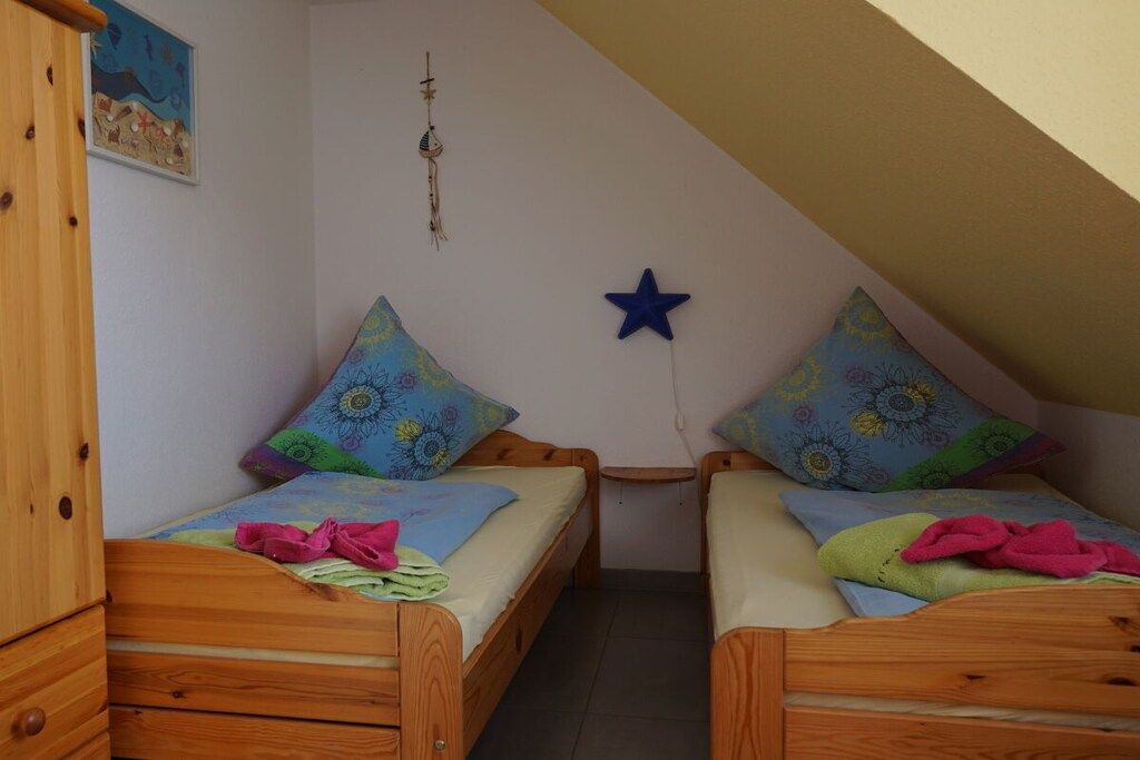 A small, cozy room with two wooden beds, each with a colorful pillow and a small bedside table.