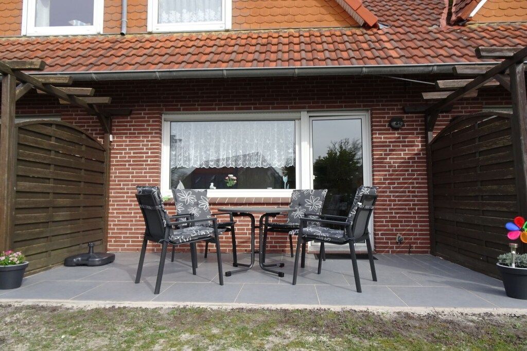 Une terrasse avec une table et quatre chaises, une maison en briques et un portail en bois.