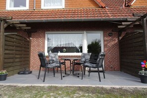 Eine Terrasse mit Tisch und vier Stühlen, ein Backsteinhaus und ein hölzernes Tor.