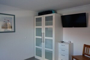 Ein Zimmer mit einem weißen Kleiderschrank, einem flachbildfernseher an der Wand und einem gerahmten Bild.