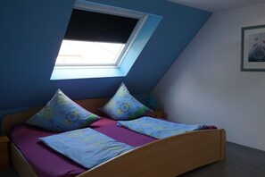 A bedroom with a sloped ceiling, a skylight, a bed with patterned pillows, and a nightstand with a lamp. - Holiday home in Norddeich with Wi-Fi (Norddeich)