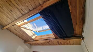 Une pièce dotée d’un plafond en bois incliné et d’un puits de lumière agrémenté de rideaux.