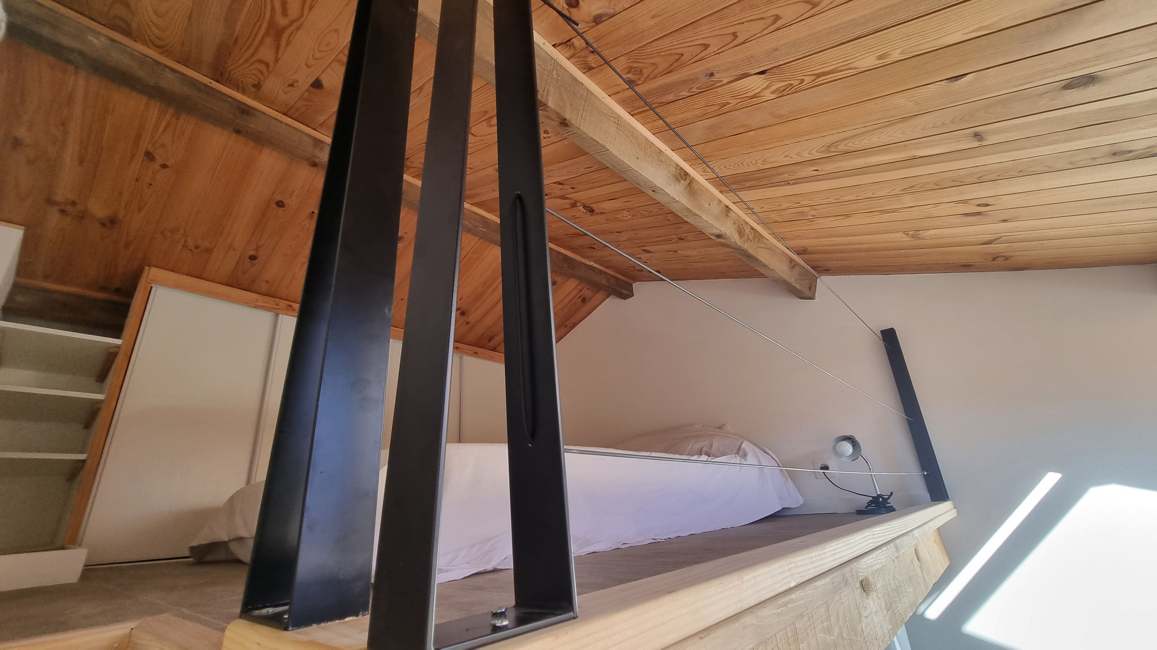 Un plafond en bois à pente douce, un lit avec une literie blanche et une porte blanche.