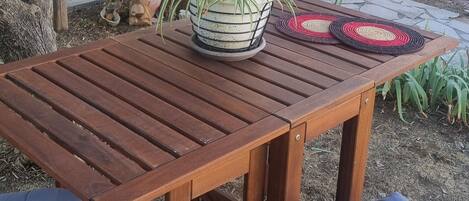 Une table en bois, un pot de fleurs, deux chaises rembourrées et un set de table en fibres tressées.