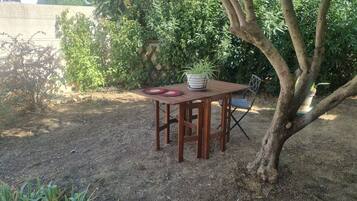 Une table en bois placée à l’extérieur, avec un pot de fleurs, une chaise et un set de table rouge.