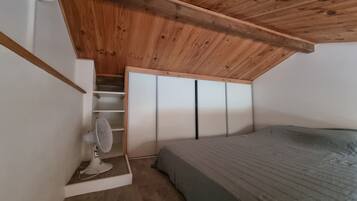 Een slaapkamer met een schuine kap, een bed, een ventilator en een kledingkast met schuifdeuren.
