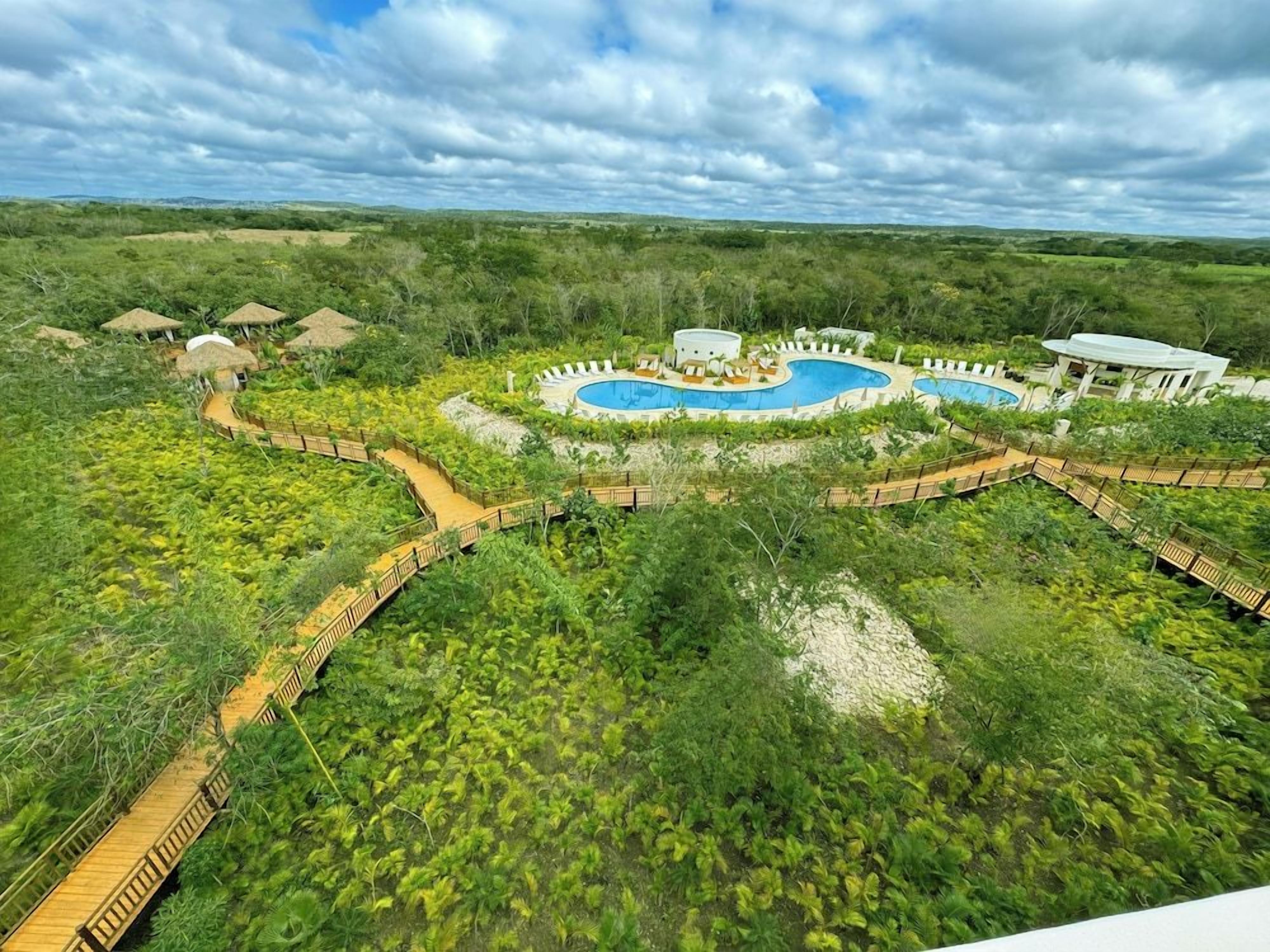 A resort with a large pool, wooden walkways, and thatched-roof huts.