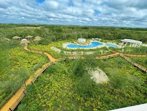A resort with a large pool, wooden walkways, and thatched-roof huts.
