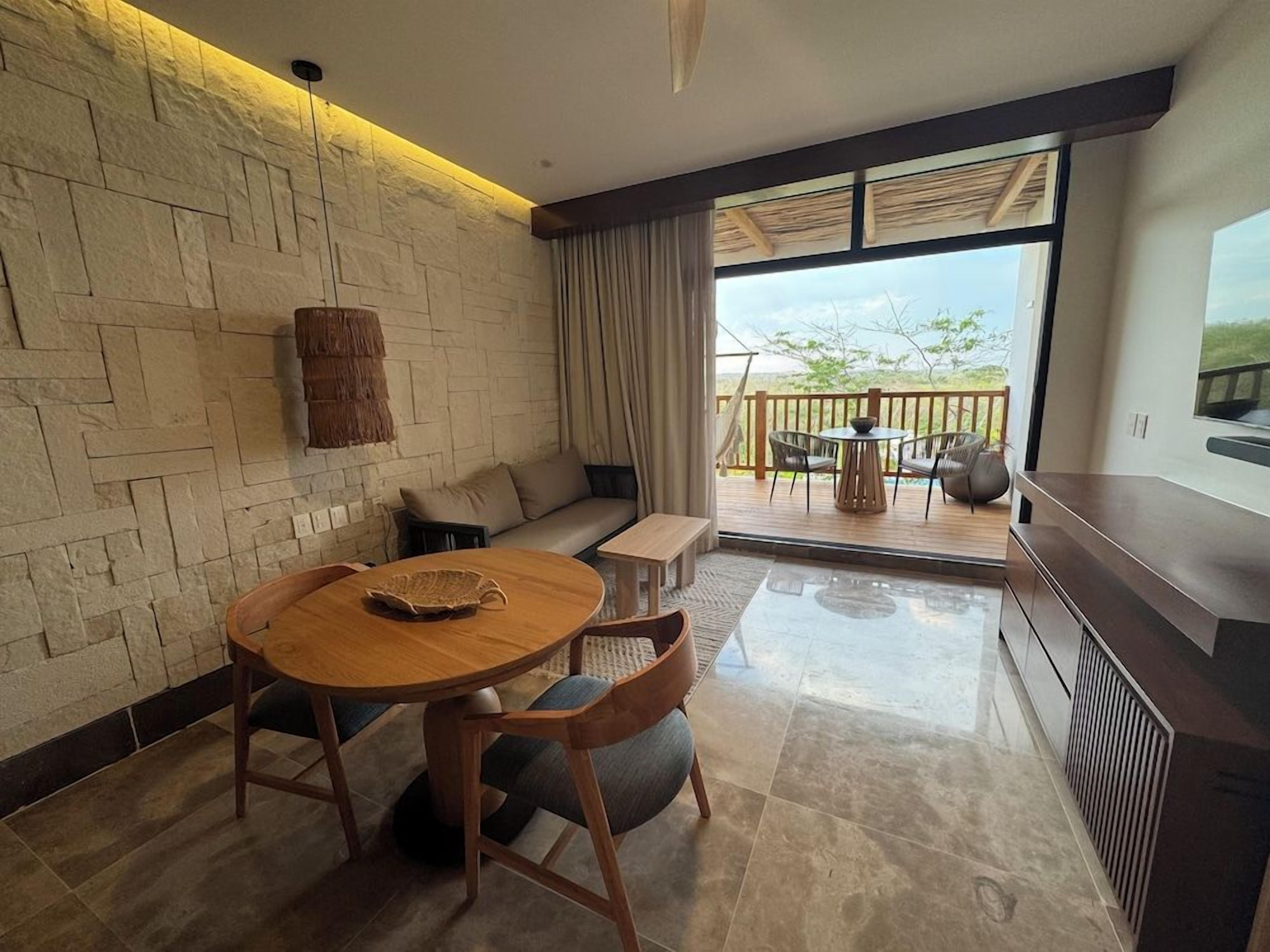A modern living room with a stone wall, a round wooden table, a sofa, and a balcony with outdoor furniture.