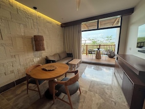 A modern living room with a stone wall, a round wooden table, a sofa, and a balcony with outdoor furniture.