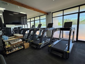 A gym with treadmills, exercise equipment, and a TV screen.
