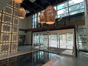 A lobby with a modern design, featuring a patterned wall, a glass entrance, and hanging pendant lights. - Hotel Gafsacomm Tulum Aeropuerto (Mérida)