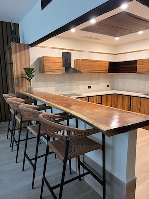 A modern kitchen with a long wooden bar counter and wicker bar stools. - Hotel Gafsacomm Tulum Aeropuerto (Mérida)