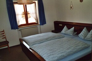 A bedroom with a double bed, two pillows, a wooden headboard, a chair, a window with curtains, and a wall-mounted light fixture. - Holiday apartment with 1 bedroom (Bad Bayersoien)