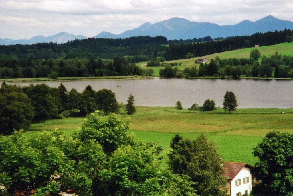Un lac entouré de verdure, avec des montagnes en arrière-plan.