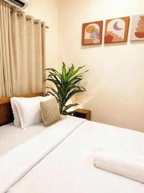 A hotel room with a bed, a potted plant, and artwork on the wall.