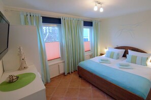 A bedroom with a bed, curtains, a nightstand, a lamp, and a wall decoration. - Dune grass with balcony (Dahme)