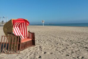 A beach chair with a striped umbrella, a lifeguard tower, and a clear sky. - Dune grass with balcony (Dahme)