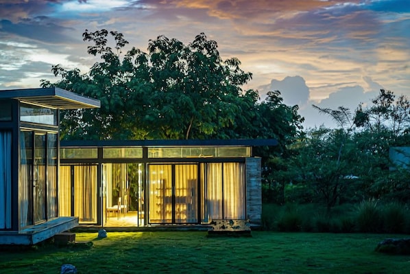 Una casa moderna con amplios ventanales, una terraza de madera y un exuberante jardín.