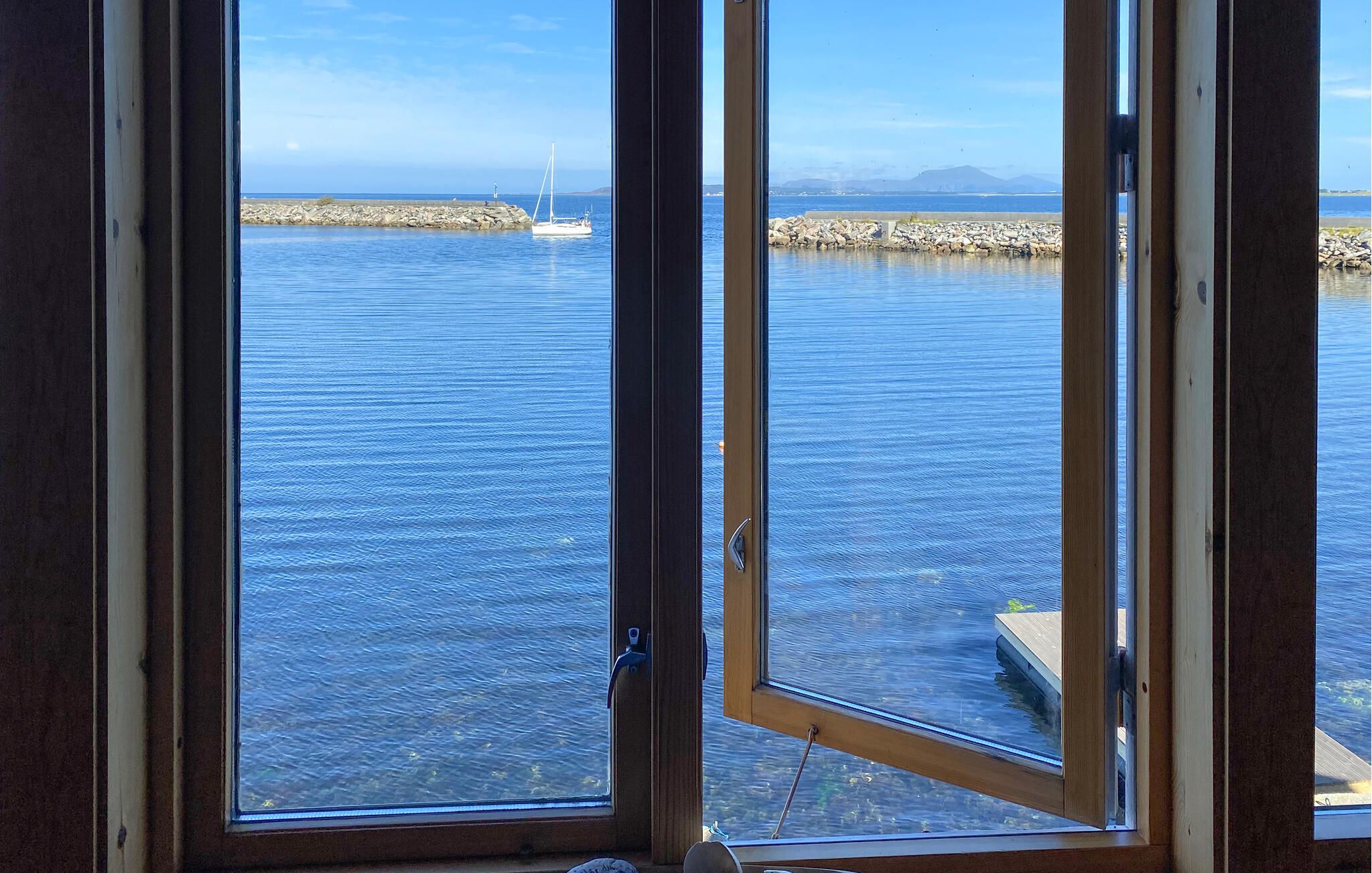 Vista a través de una ventana de un cuerpo de agua tranquilo con una costa lejana y un velero.