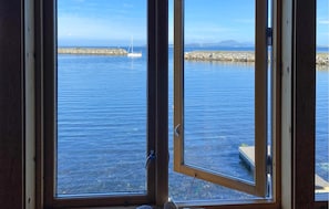 Blick durch ein Fenster auf ruhiges Wasser mit einer fernen Küstenlinie und einem Segelboot.