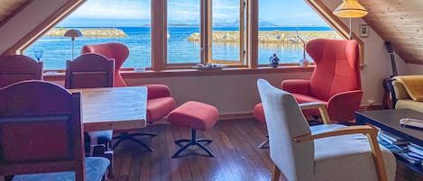 A cozy room with a large window overlooking a body of water, wooden flooring, and red and white furniture.