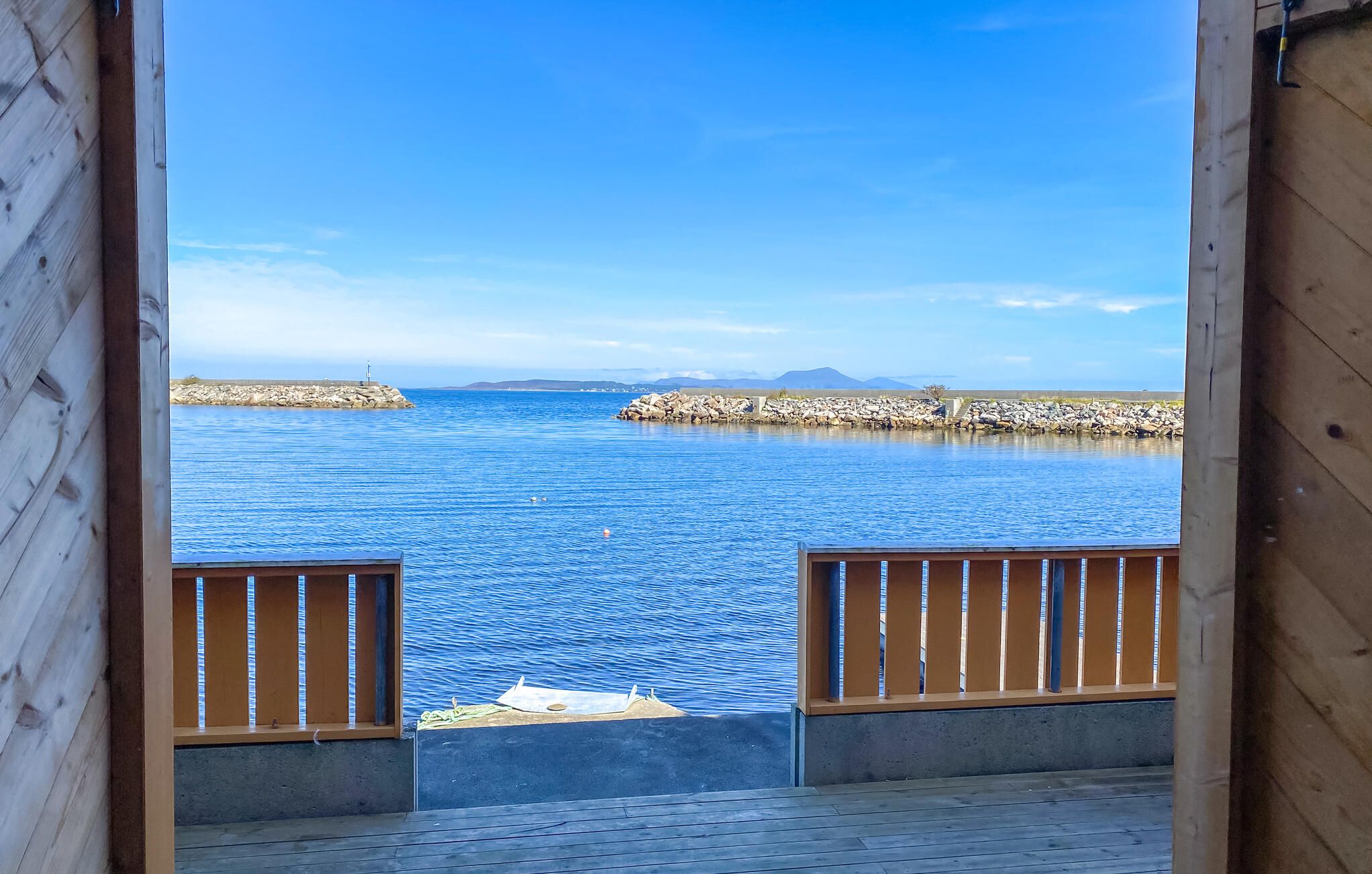 A wooden deck with a view of a calm sea and rocky breakwaters.