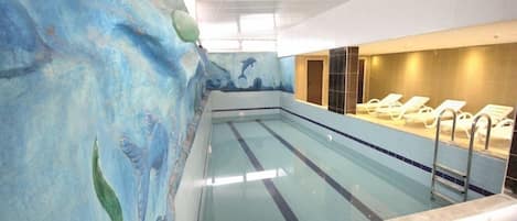 An indoor swimming pool with a dolphin mural on the wall, a changing room area with benches, and a tiled floor.