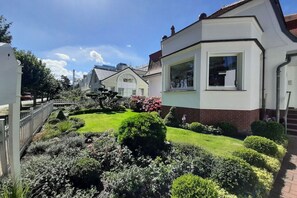Un quartier résidentiel doté d’un jardin bien entretenu, une maison avec une grande fenêtre et un immeuble voisin qui se distingue par son toit particulier.