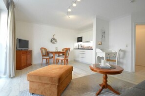 A compact living space with a kitchenette, a dining area, and a seating area with a small table and ottoman. - Villa Steinfurth Ap 1 (Ostseebad Binz)