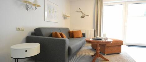 A modern living room with a grey sofa, a round side table, a small wooden coffee table, and a patterned rug.