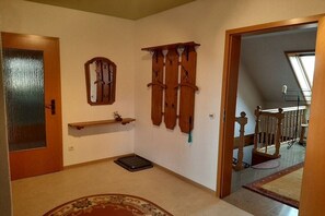 A hallway with a wooden door, a small shelf, a wall-mounted coat rack, and a staircase leading to an upper level. - Holiday apartment with 1 bedroom (Annaberg-Buchholz)