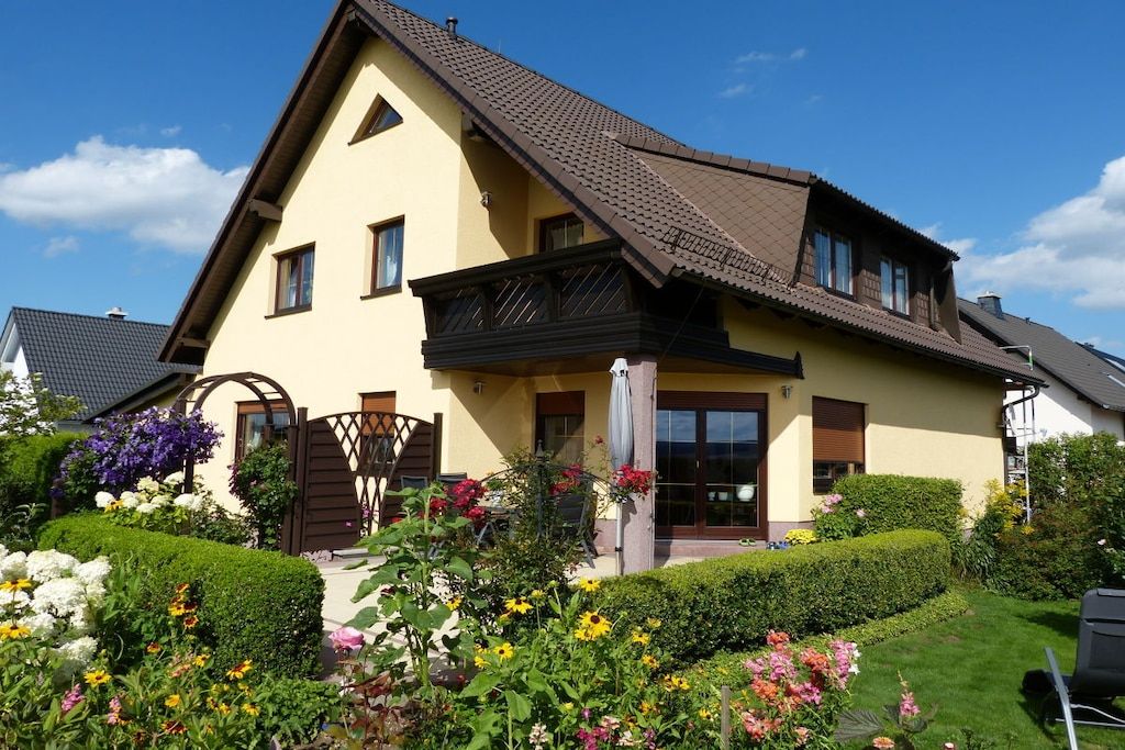 A two-story house with a sloped roof, a front porch, and a well-maintained garden with various flowers and shrubs.