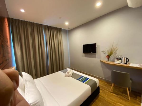 A hotel room with a bed, a desk, a chair, a television, and a window with curtains.