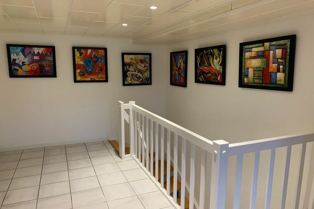 A hallway with a white railing and six abstract paintings on the wall.