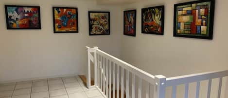 A hallway with a white railing and six abstract paintings on the wall.