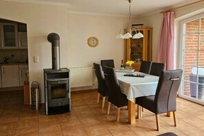 A dining area with a table, chairs, a stove, a clock, and a window with a view. - Holiday home in Norden with swimming pool (Norden)