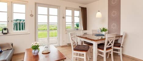 A dining area with a table and chairs, a sofa, and a view through the windows.