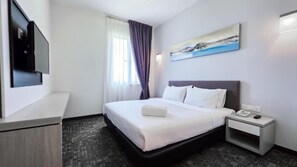 Quarto de hotel com cama, mesa de cabeceira com telefone, televisão de tela plana na parede e janela com cortinas.
