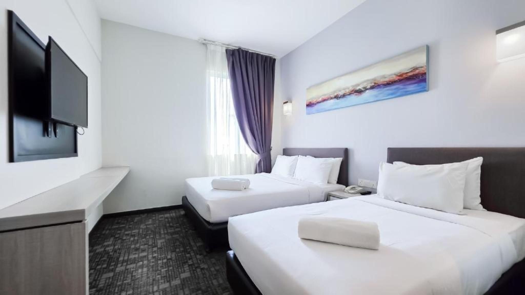 A hotel room with two beds, a flat-screen TV mounted on the wall, a painting above the beds, and a window with curtains.