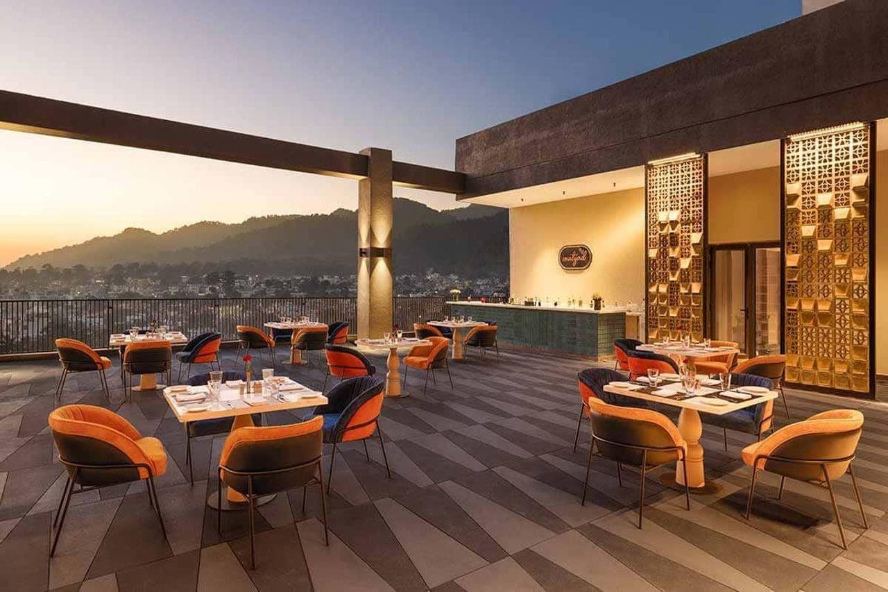 An outdoor dining area with tables and chairs, a bar, and a view of a cityscape.