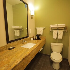A bathroom with a granite countertop sink, a mirror, a toilet, and towel racks. - Spark by Hilton Harrisburg East (Harrisburg)