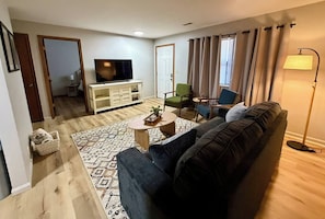 Ein Wohnzimmer mit einem dunklen Sofa, einem Couchtisch, einem Fernseher und einer Lampe.