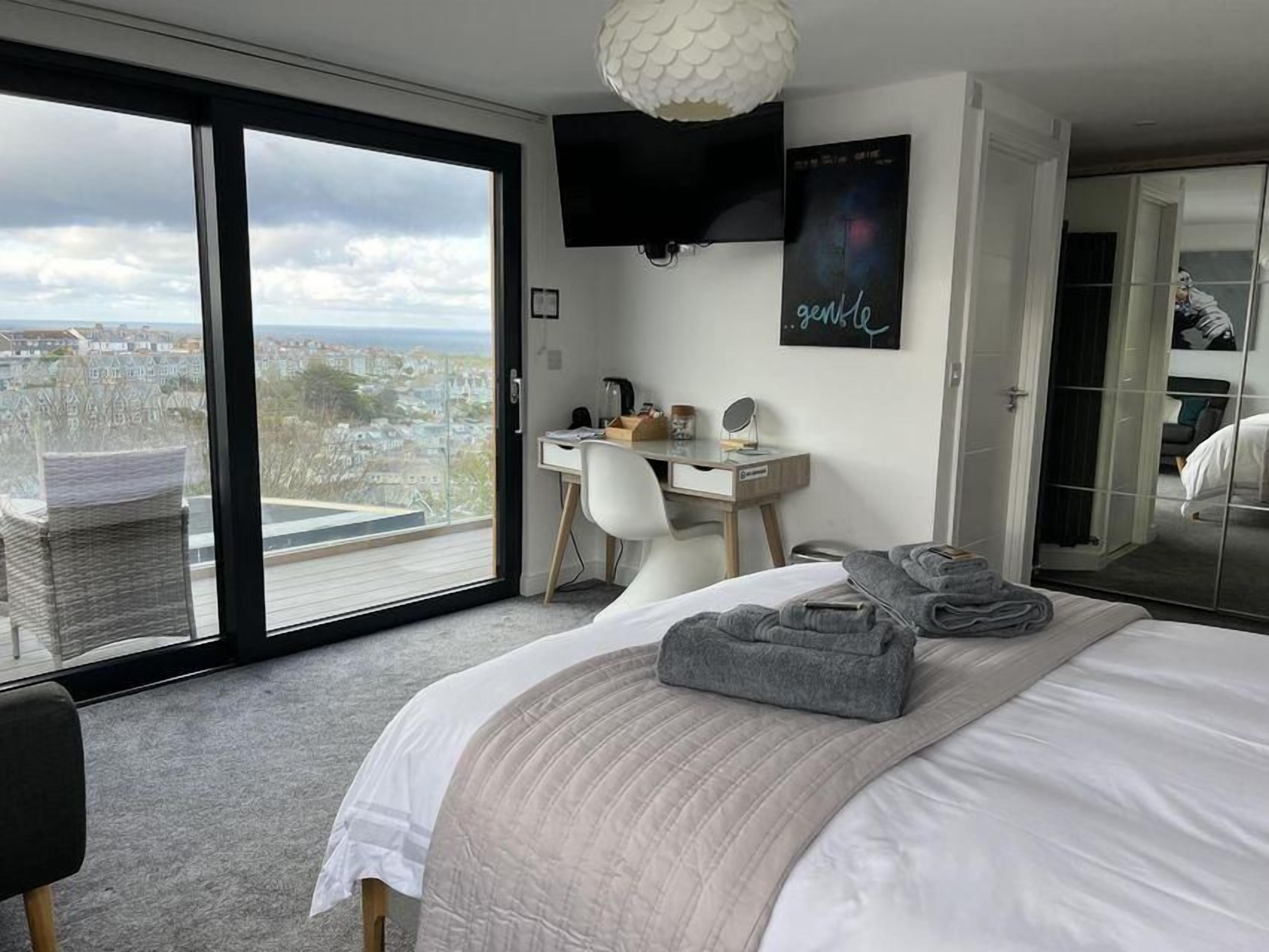 A bedroom with a large bed, a desk, a chair, and a view through a sliding door.