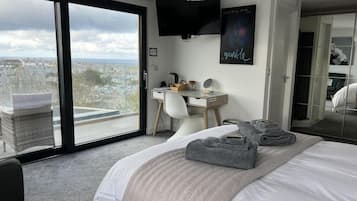 A bedroom with a large bed, a desk, a chair, and a view through a sliding door.