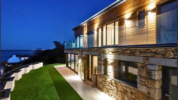 A modern house with a stone facade, a wooden deck, and a view of the sea.