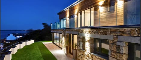A modern house with a stone facade, a wooden deck, and a view of the sea.